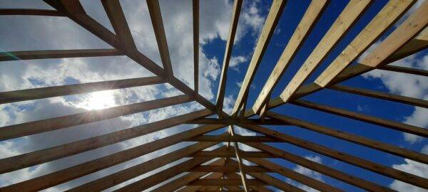 An upward view of a geometric steel framework of an under-construction building, converging into the blue sky with fluffy clouds, representing the ambitious architectural projects undertaken by PF & CO Construction.